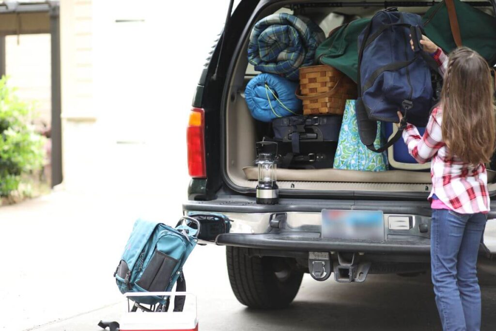 Young girl packing the trunk of an SUV for a camping trip