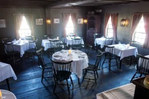 Elegant dining setup inside the historical White Horse Tavern in Newport RI, showcasing tables with white linen and wooden chairs on a vintage wooden floor.
