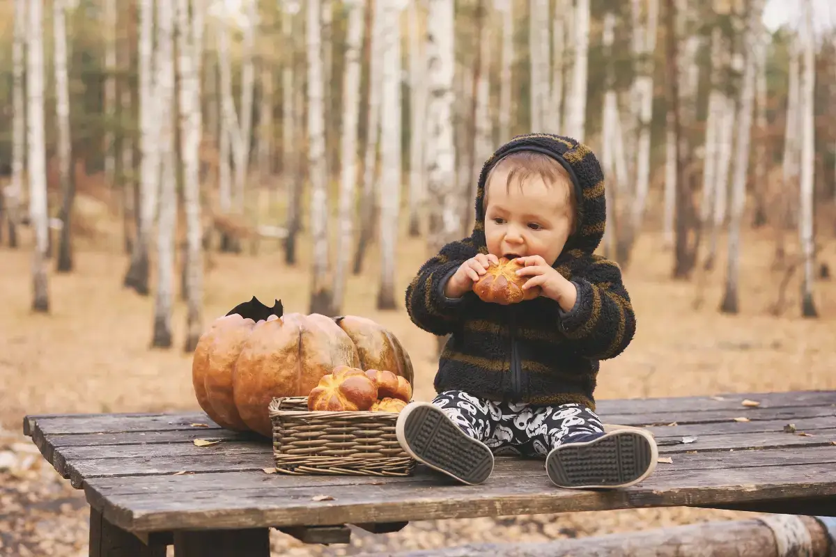 Baby sitting at a picnic table with pumpkins in an autumn forest, enjoying things to do in Mystic CT in October.