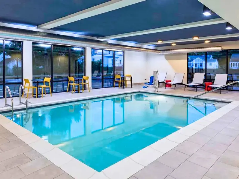 Indoor pool at Home2 Suites near New Haven with lounge chairs and tables.