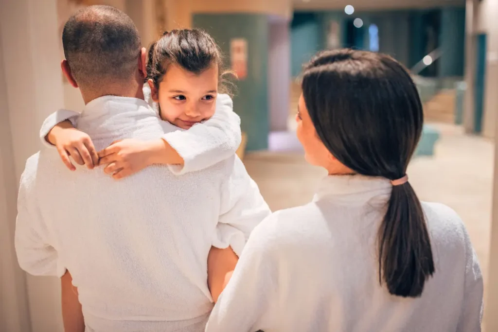 Young girl smiling in her dad’s arms with parents wearing hotel robes at one of the best New Haven hotels.