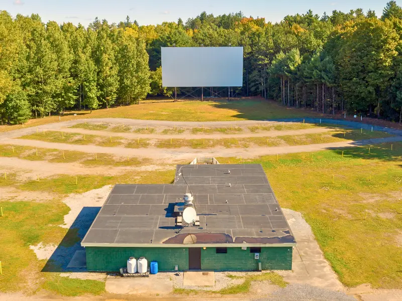 Empty drive-in movie theater during the day with screen and trees in background