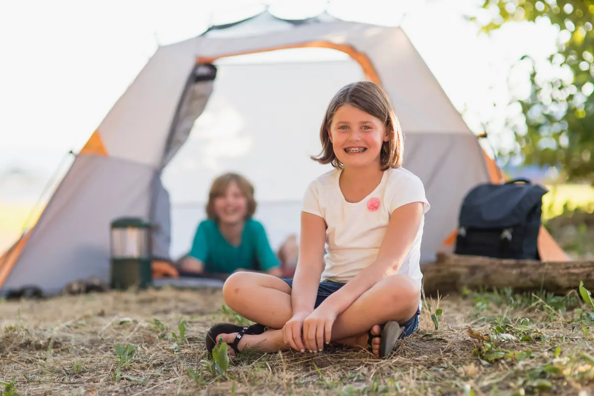 Smiling kids outside a tent while camping.