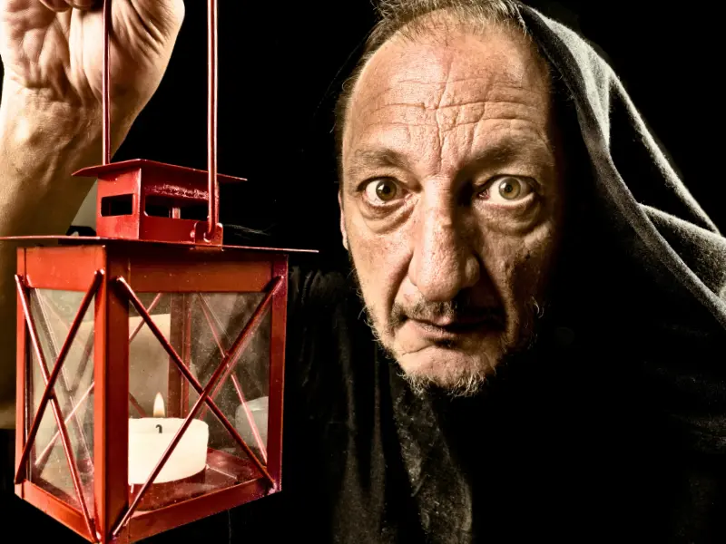 A man holding a candle lantern during a spooky museum tour.