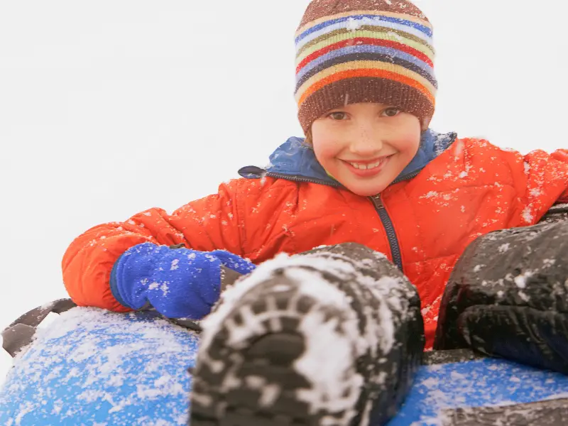 Child in winter gear smiling while snow tubing at Powder Ridge
