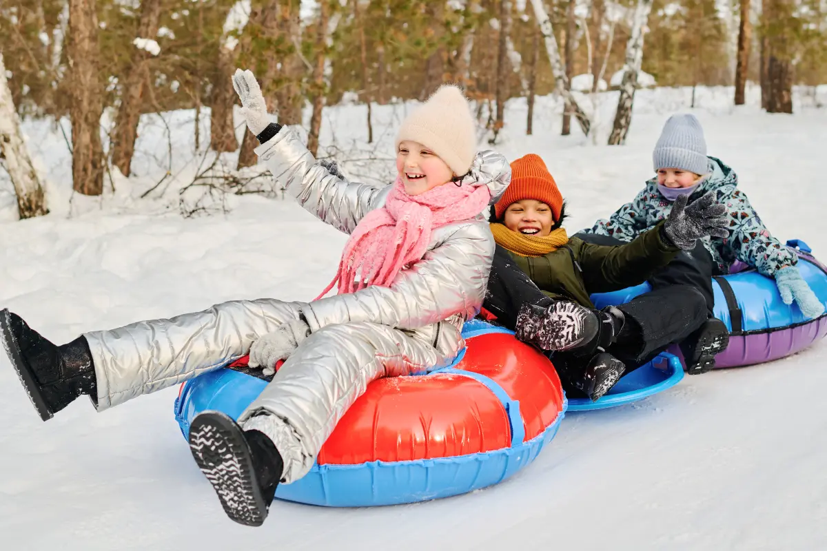 Kids riding linked snow tubes on a wooded snow tubing trail