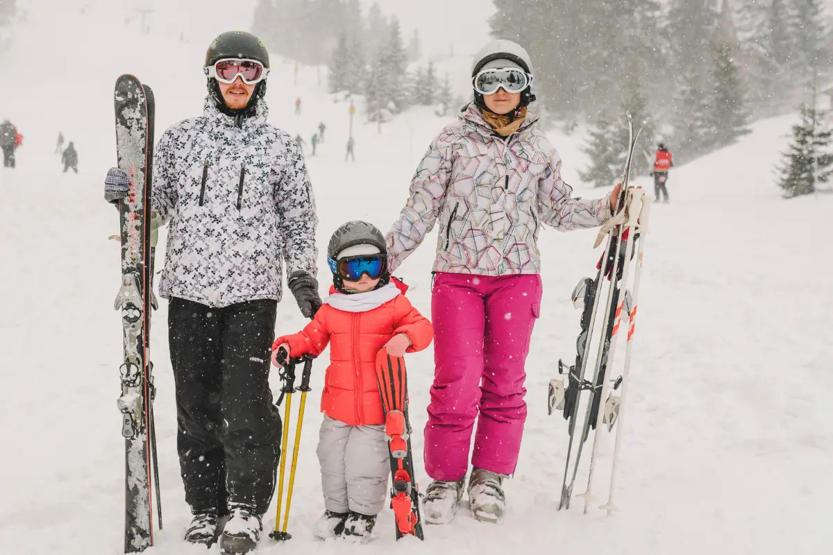 Family with toddler walking through snow carrying skis at a ski resort