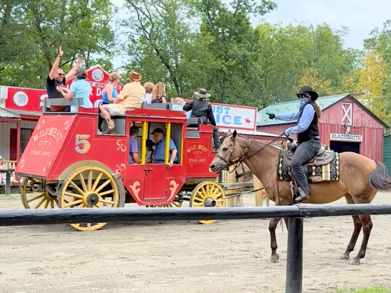 Visitors riding a red stagecoach while a cowboy on horseback rides beside it at Wild West City in New Jersey