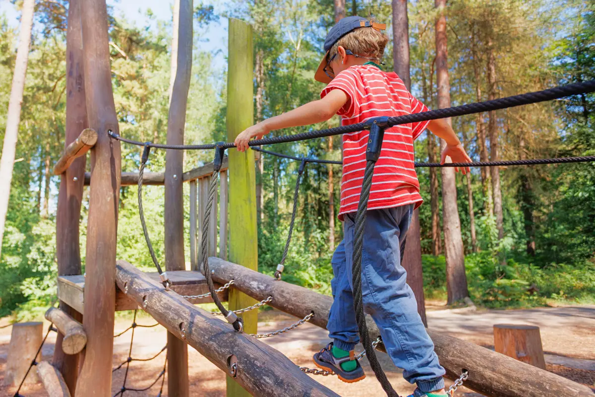 Child balancing on rope bridge at wooden playground during summer