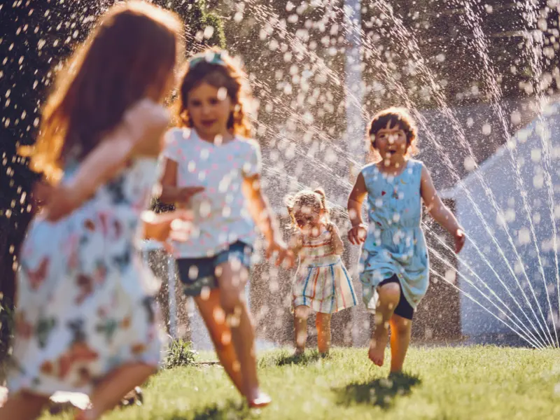 Kids running through a sprinkler, giving 90s summer day vibes