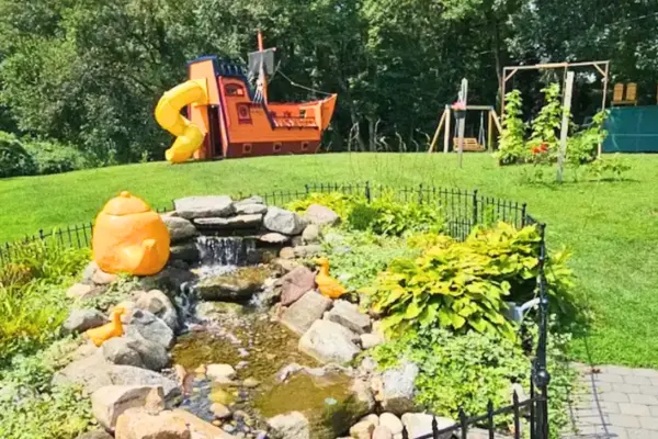 Garden area with small waterfall and playground at Crepes Tea House in Southwick with outdoor seating and greenery