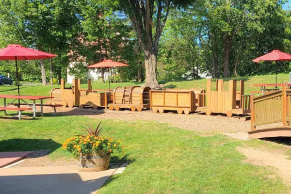 Wooden train playground at The Summer House in Southwick with picnic tables and shaded outdoor seating